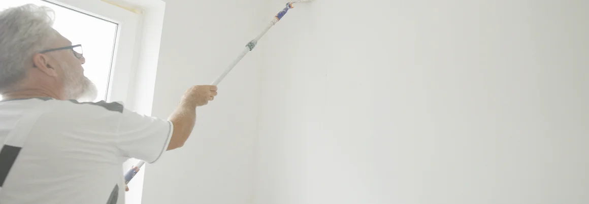 Person bringt mit einem Kleisterroller Kleister direkt auf der Wand an.